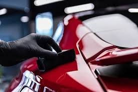 Gloved hand applying coating to glossy red car surface in a garage.
